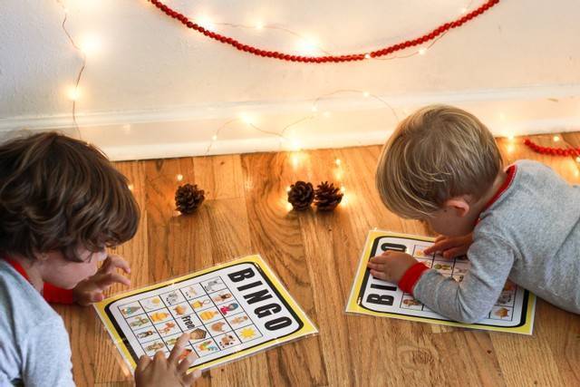 2 small boys laying under Christmas lights playing nativity bingo